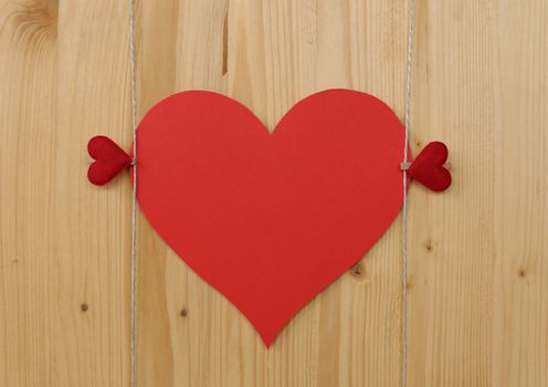 Two hearts with clothes pegs and red paper heart on a cord on wood