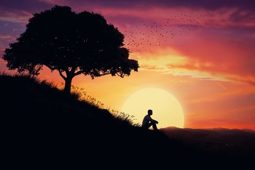 Boy sit alone on a hill in the center of nature, over a sunset background. Standing away from the crowd, waiting for the healing power of the nature.