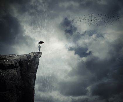 Man with an umbrella stand on the edge of the cliff, calling the rain. Mysterious place above the clouds.