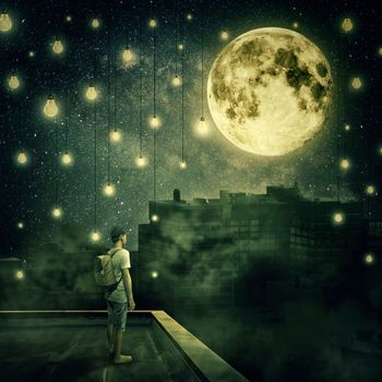 Young boy stay on the rooftop looking at the full moon. Mysterious night with suspended lightbulbs as stars over the foggy city