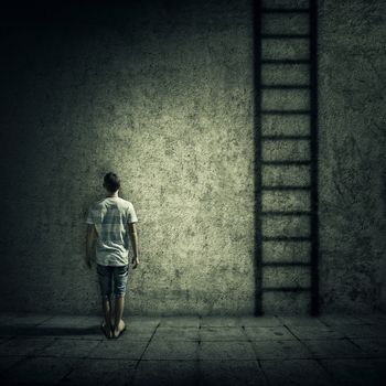 Abstract idea with a person standing in a dark room, in front of a concrete wall, figuring a ladder to escape. Surrounded by limitations, daily routine.