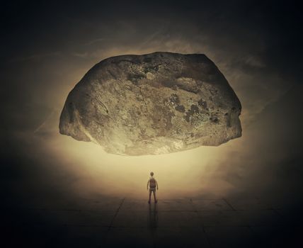 Surrealistic image as a man, with a bag in his back, stand in a foggy street below a huge squeezing rock. Life pressure and stress concept.