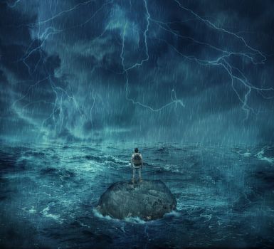 Lost man standing abandoned on a rock island in middle of the ocean, in a stormy night with lightnings in the sky. Looking for help, trying to survive. Adventure, journey and hard determination concept.