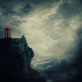 Surreal view as a sad, young man, standing on the edge of a cliff near a red telephone box, waiting someone to call him.