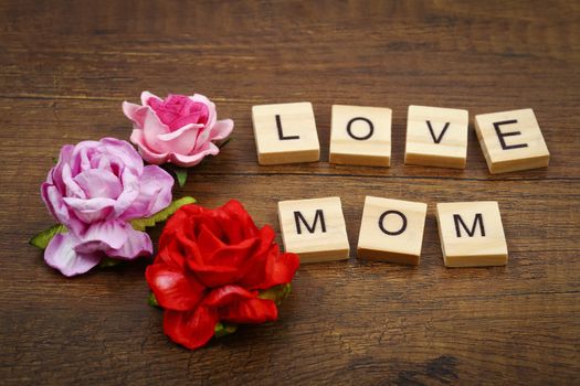Love mom wording with pink rose flowers on old wooden textured background, Mother's day concept.