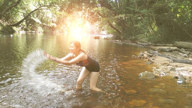 Beautiful girl is playing a river , river surrounded by tropical forest  , with warm sunlight effect.