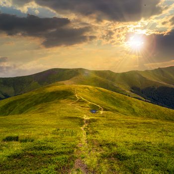 small lake near mountain curve path on a Green Hill at sunset