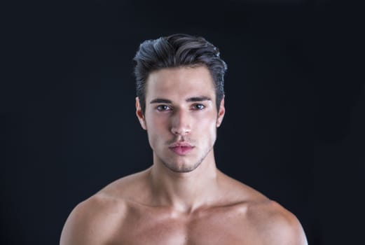 Handsome, fit young man wearing only underwear standing isolated on black background, looking at camera