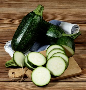 Arrangement of Fresh Ripe Zucchini Full Body and Slices on Cutting Board closeup on Wooden background