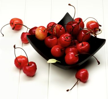 Arrangement of Sweet Maraschino Cherries in Black Wooden Plate closeup on White Plank background