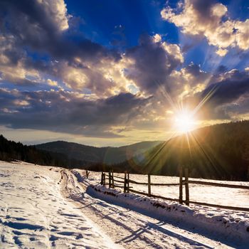 winter mountain landscape. winding road that leads into the pine forest covered with snow. wooden fence stands near the road at sunset