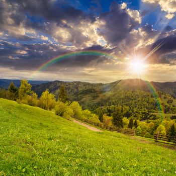 autumn landscape. fence near the meadow path on the hillside. forest in fog on the mountain at sunset