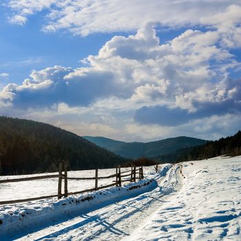 winter mountain landscape. winding road that leads into the pine forest covered with snow. wooden fence stands near the road.