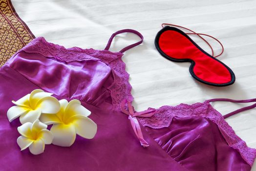 Silk pajamas, eye mask and frangipani on the bed close up