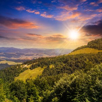 slope of mountain range with coniferous forest and village at sunset