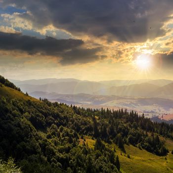 slope of mountain range with coniferous forest and village at sunset