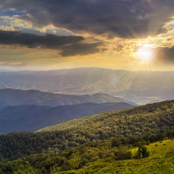 slope of mountain range with coniferous forest and village at sunset