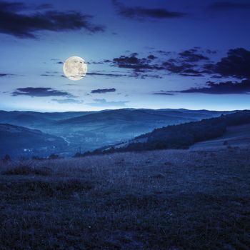 Stack of hay on a green meadow in the mountains in the morning under a blue summer sky at night in full moon light