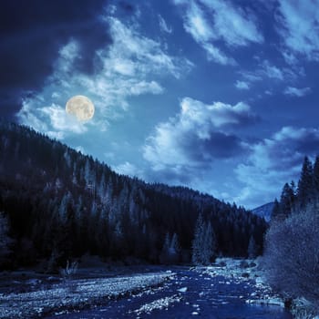 mountain river with stones in the forest near the mountain slope at night in full moon light