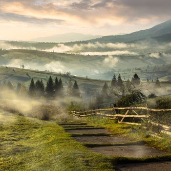 stone steps down the hill in to village in foggy mountains at sunrise