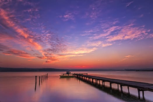 Stunning water reflection sunset with wooden pier and boat