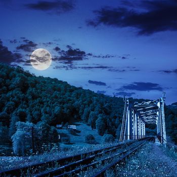 old railroad passes through the metal bridge in the mountain village at night in moon light