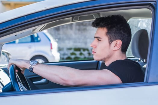 Serious young man or teenager driving car and looking at camera