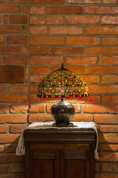 table lamp of stained-glass on old wooden stand on red brick wall background