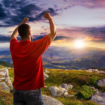 man in red shirt standing in sunlight on stone mountain slope with forest at sunset