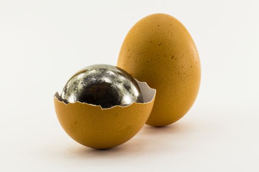 Rusty steel ball inside the shell of chicken egg and one whole chicken egg isolated on white background