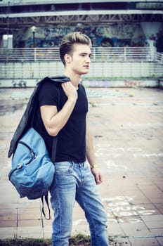 Attractive young man standing in city environment, with rucksack on one shoulder