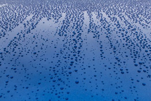 Many drops of water on a blue surface. Traces of rain on the hood of the car.