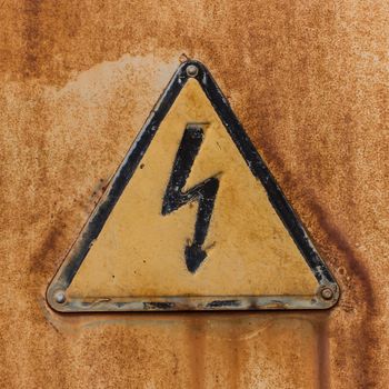 Old triangular High Voltage sign attached by rivets to a sheet of rusty iron.