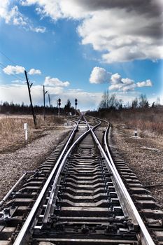 Railway bifurcation in north-west of russia in early spring. Blue sky with white clouds. A very cold windy day.
