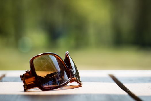 Sunglasses on the table in the sun on a wooden table in the background of a spring forest
