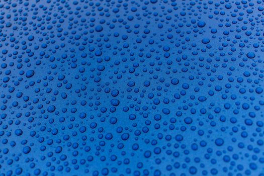 Closeup of rain drops on a blue smooth metal surface. Background or texture.