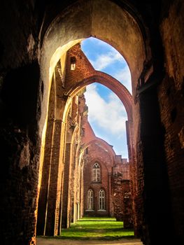 The ruins of the Gothic cathedral of red brick with blue sky and green grass