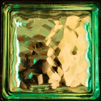 Green square glass block close up. Building material. Element of the wall. Refraction of light inside a glass object creates an interesting effect.