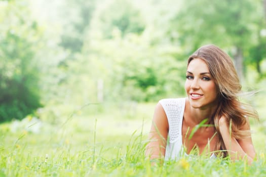Beautiful young woman in white dress lying on grass