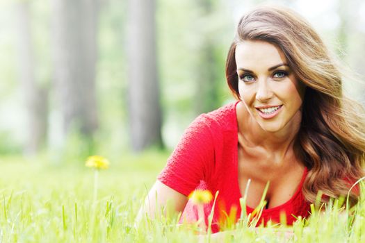 Beautiful young woman in red dress lying on grass