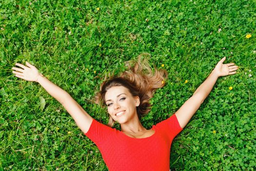 Beautiful young woman in red dress lying on grass, top view