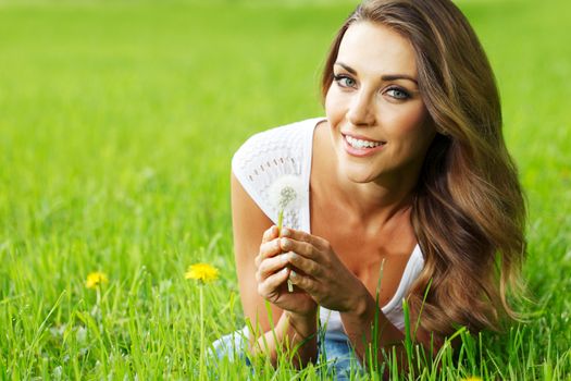 Beautiful young woman with dandelion lying on grass