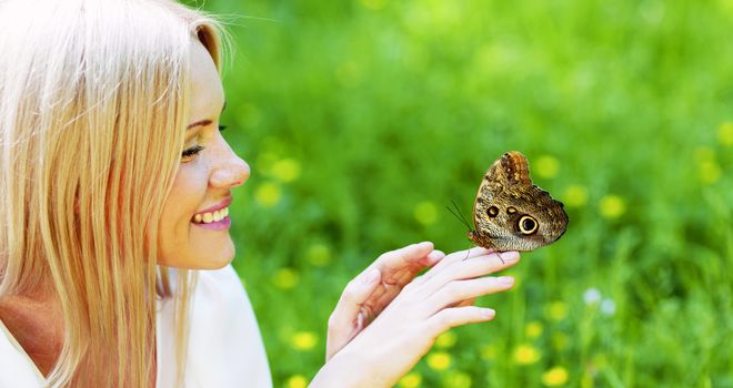 Woman playing with a butterfly on green grass