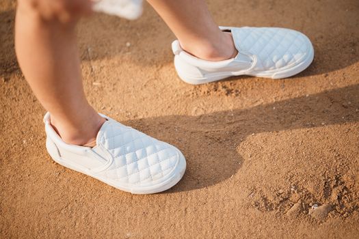 Female feet in sneakers on the sand