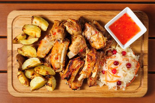 big wooden board with fried pork ribs, baked potato, hot sauce and sauerkraut, preferably served as companion for beer or other alcool drinks