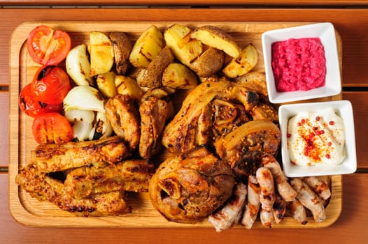 big wooden board with pork ribs and steaks baked in mustard sauce, small sausages, baked potato, grilled tomatoes and onion, hot sauce and horseraddish sauce, preferably served as companion for beer or other alcohol drinks
