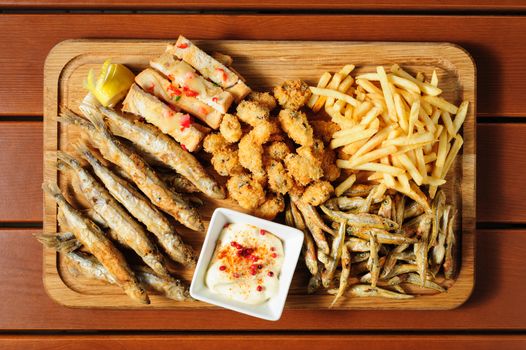 big wooden board with fried fush, mussels, french fries served as companion for beer or other alcool drinks, top view