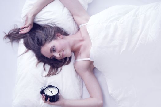 Young beautiful woman waking up with alarm clock