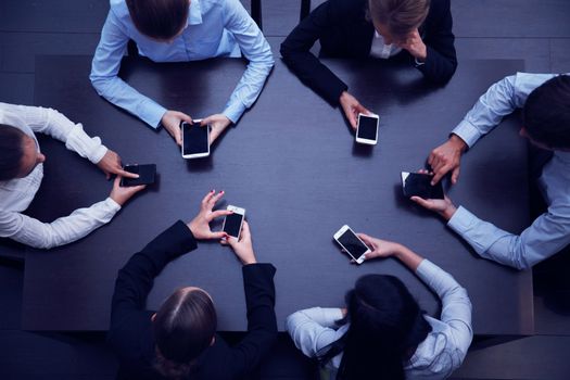Business people with smartphones sitting around the table, top view