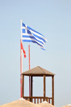 Greek flag floating on a white mat near a guard post on the beach of Amoudara on the island of Crete